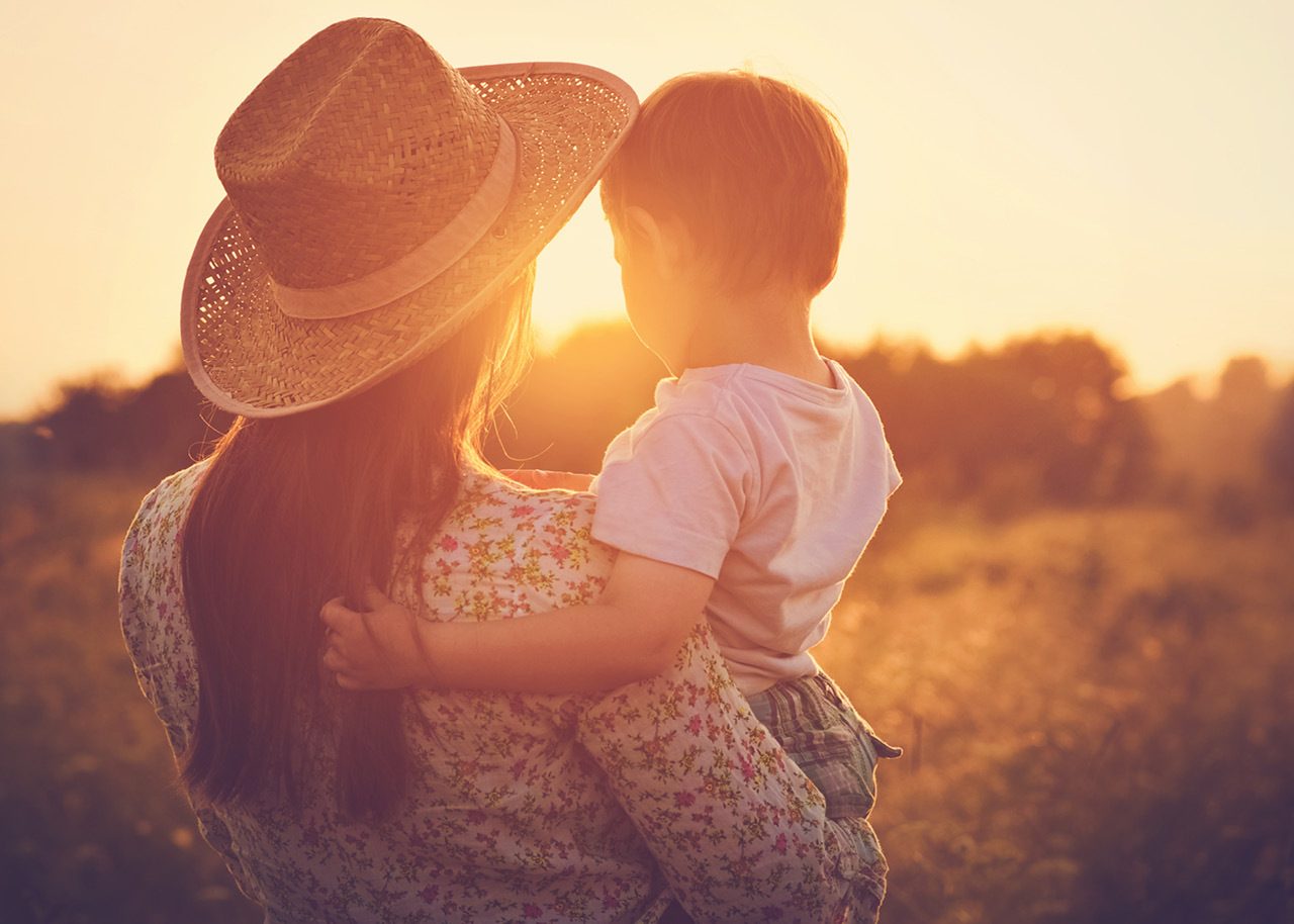 Image of mother holding toddler son in a field at sunset